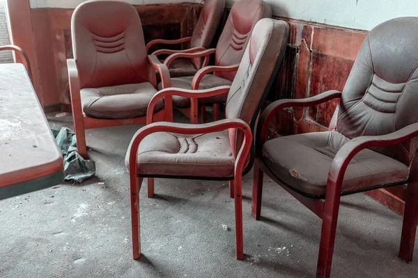 在一座废弃的大楼里 红色的办公椅围绕着尘土飞扬的桌子进行着特写镜头 — 图库照片