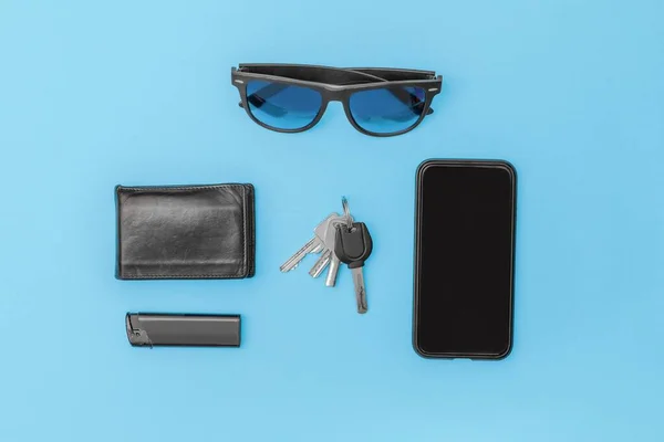 現代人の項目のトップビュー テーブルの携帯電話のサングラス軽量財布キーで黒で青の背景 — ストック写真
