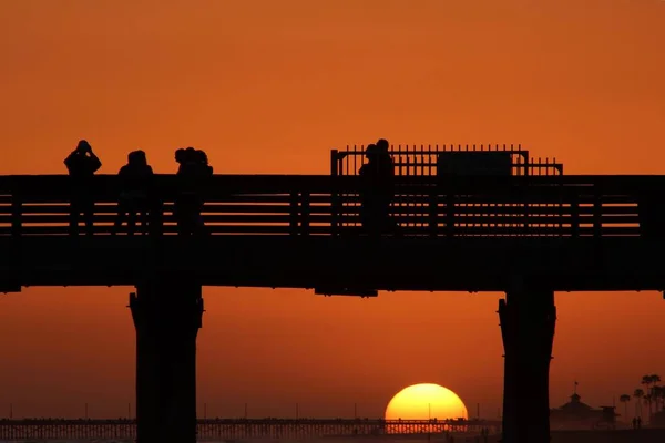 橋のシルエットと夕日を背景に美しいオレンジ色の太陽と一緒に歩いている人々 — ストック写真