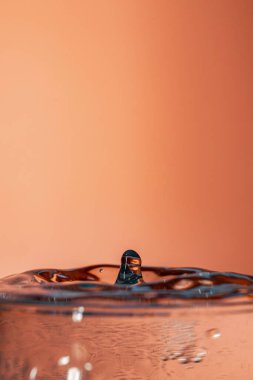 Şeftali arkaplanına sıçramış tek bir damla suyun dikey yakın çekimi.