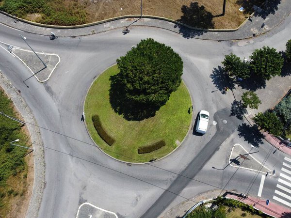 An aerial view of a tree in a traffic circle with a car on the road