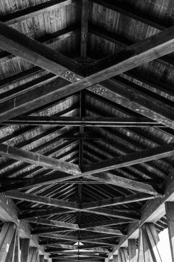 İçeriden uzun tahta bir çatının dikey gri tonlu görüntüsü.