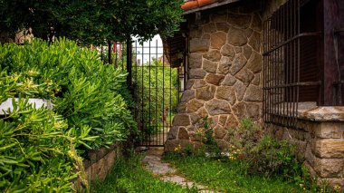 Yeşil arka bahçeli metalik pencere parmaklıkları olan güzel bir taş bina manzarası.