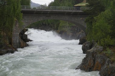 Norveç, Oslo 'da büyük kayalar ve ağaçlarla çevrili bir nehir üzerindeki kemer köprü.