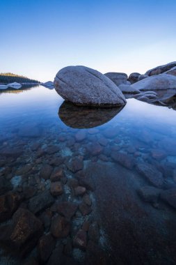 Gökyüzünün yansımasıyla büyük kayalar ve berrak bir göl.
