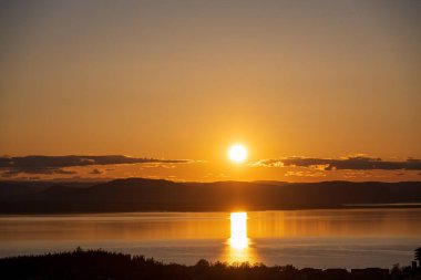 Tepe siluetleriyle gölde yansıyan resimli bir günbatımı gökyüzü
