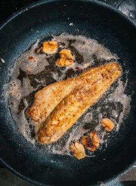 Sıcak tavada yağlı, cızırdayan balık filetosunun dikey görüntüsü.