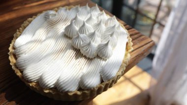 Beyaz kremayla kaplı lezzetli bir limonlu turta ahşap bir masanın arka planında.