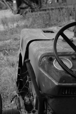 Kırsal bir alanda terk edilmiş eski bir traktörün dikey siyah beyaz görüntüsü.