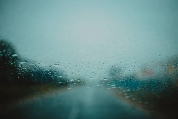 背景に水滴やぼやけた道を持つ濡れた車のフロントガラス — ストック写真