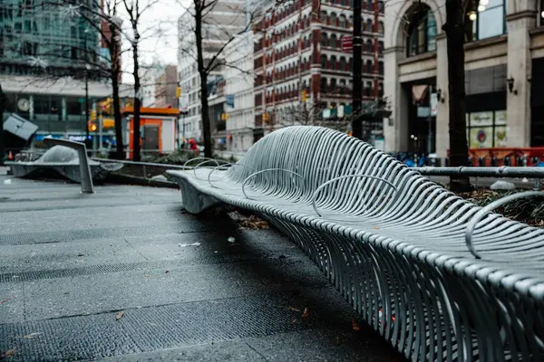 雨のニューヨーク市の近代的な建物のある通りに抽象的な金属製のベンチ — ストック写真