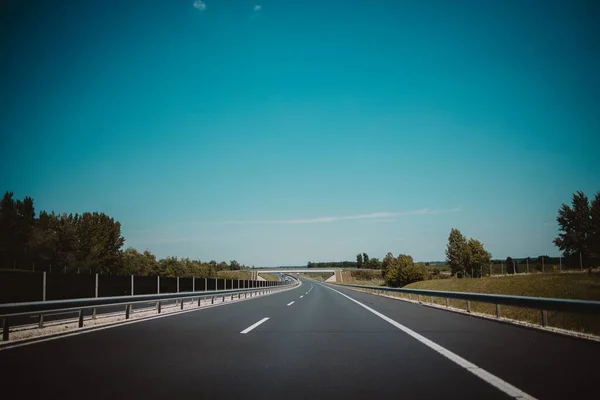 Egy Üres Országút Fehér Jelzésekkel Korlátokkal Zöld Fákkal Mellette Kék — Stock Fotó