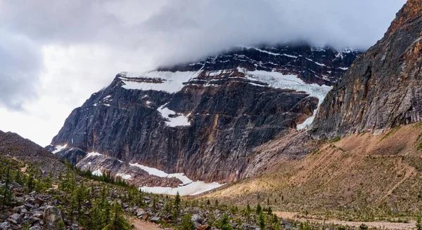 Uma Montanha Rochosa Com Pouca Neve Com Nuvens Cobrindo Pico — Fotografia de Stock