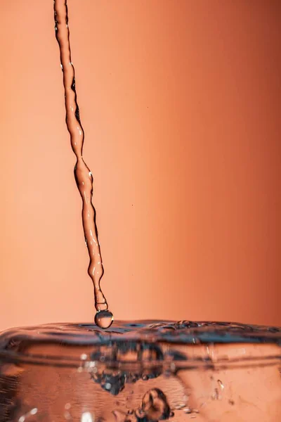 Вертикальный Кадр Наливания Жидкости Брызг Поверхность Оранжевом Фоне — стоковое фото