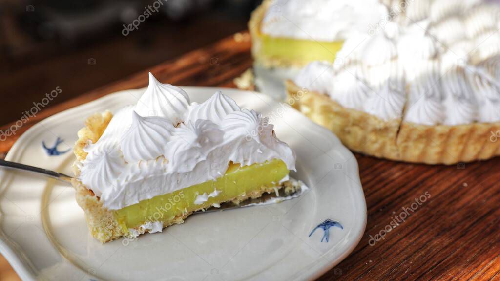 A sliced delicious lemon tart topped with white whipped cream against a background of a wooden table