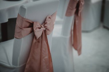Bir etkinlikte beyaz örtülü ve pembe kurdeleli dekoratif sandalyelerin yakın çekimi.