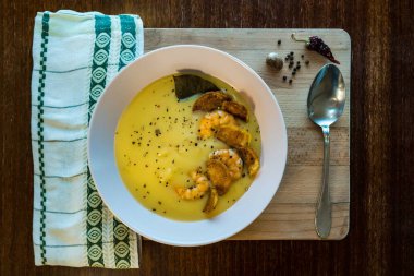 Tahta sunucuda karides ve yanında kaşık olan patates çorbası manzarası.