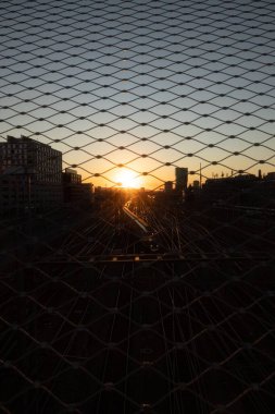 Ufuk çizgileri siluetleri olan bir çitten gün batımı manzarası ve demiryolu, Zürih, dikey çekim.