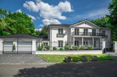 Güneşli bir günde mavi gökyüzünün altında yeşil çimenli lüks bir beyaz ev.