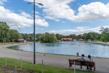 South Marine Park, South Shields, İngiltere 'deki göl manzarası. Genç bir çift bankta oturuyor..