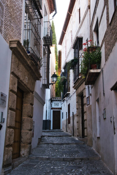 A vertical of narrow walkway in Granada, Spain with close residential buildings and a bumpy path