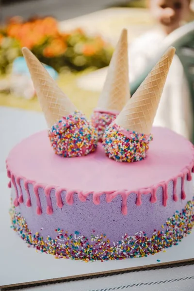 一个粉色和紫色的滴滴蛋糕 上面有松饼圆锥 上面有洒水 垂直射击 — 图库照片