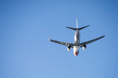 Arka planda açık mavi gökyüzü ile havalanan bir uçağın düşük açılı görüntüsü.