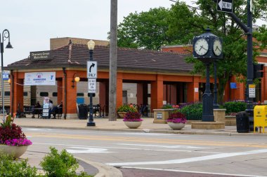 Downers Grove, Illinois Tren İstasyonu Kuzeyde sokak işaretleri, saat, ağaçlar ve çiçeklerle.