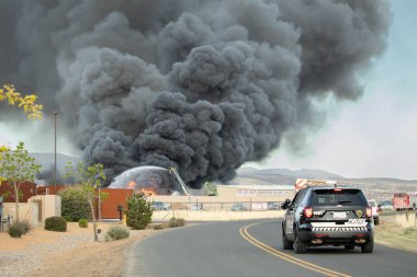 Birçok itfaiyeci arka planda yükselen dumanla mücadele ediyor. Prescott Valley Arizona 'daki bir hurdalıkta.