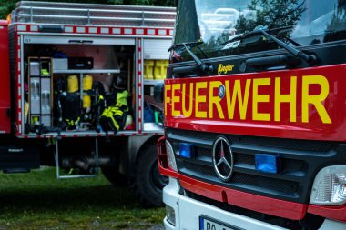 İtfaiye 'Feuerwehr' bir itfaiye arabasının üzerinde. Arka planda ikinci bir araçta teknik malzeme var..