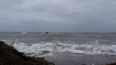 Ufukta bulutlu bir gün batımına karşı köpüklü gri deniz dalgalarının manzarası