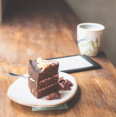 Kafe masasında bir dilim kek, kahve ve e-okuyucu tabletinin yakın plan çekimi.