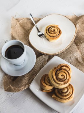 Bir fincan kahveyle tabakta üst üste dizilmiş tarçınlı rulo.