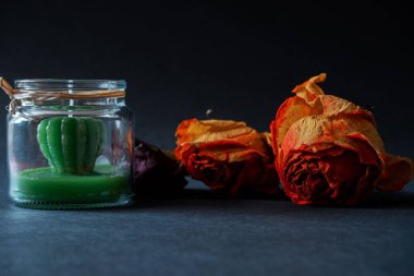 Kurumuş turuncu güllerin yakın plan görüntüsü yeşil dekoratif bir mumla bardağın yanında.