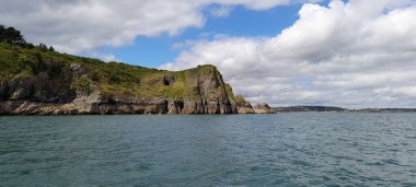 Gökyüzünde bulutlarla çevrili bir kaya adasının güzel bir görüntüsü.