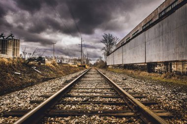 Bir bina ve bulutlu bir gökyüzü ile çevrili demiryolu manzaralı bir çekim.