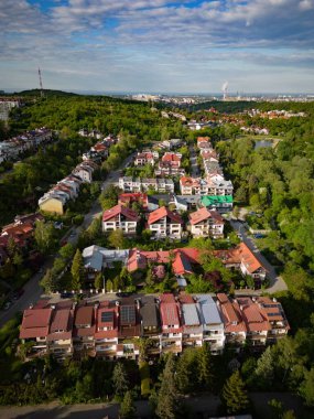 Güneşli bir günde yeşil ormanlarla çevrili bir yerleşim yerinin havadan görüntüsü.