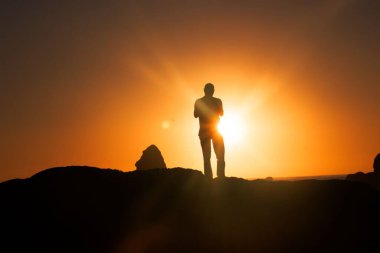 Güneşin batışının keyfini çıkarırken tepede duran bir adamın silueti.