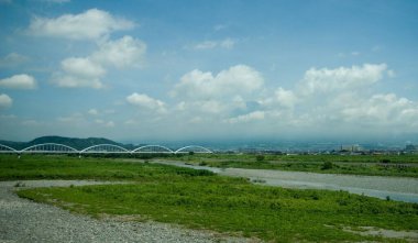 Yeşil bir tarla manzarası ve Fuji Subaru hattının arka planında bir nehir.