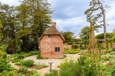 Bahçede ağaçlarla ve dekoratif bitkilerle çevrili küçük tuğla bir barakanın güzel manzarası.