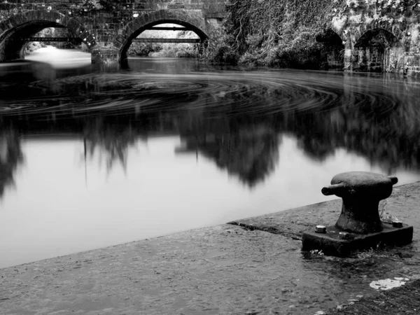 石造りの橋のある公園内の反射川のグレースケール — ストック写真