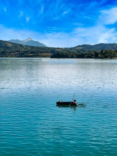 在绿山映衬下 在湖中航行的船只上一个人的垂直镜头 — 图库照片