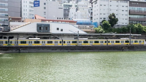 在多云的夏日 Ichigaya火车站位于一条河的沿岸 与一条黄色的洞伊地铁 新宿线列车相连 — 图库照片
