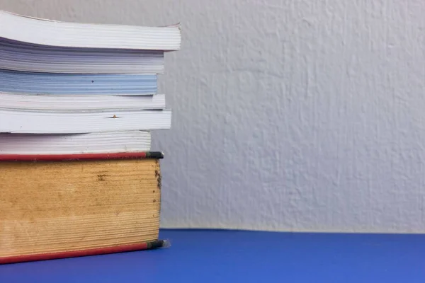 白い壁の背景に青いテーブルの上の本の山 — ストック写真