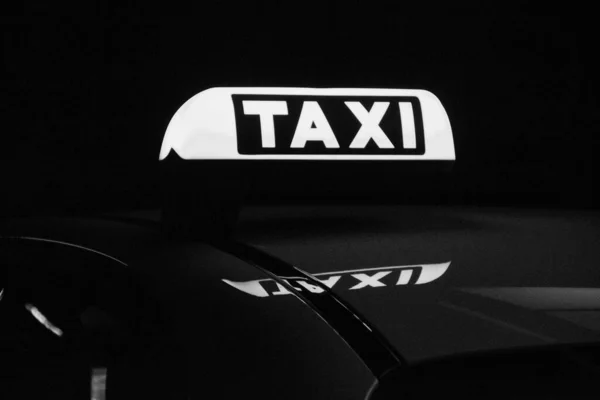 A closeup of a taxi sign on top of a black car with dark background