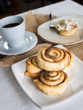 Dikey yakın plan tarçınlı çörek ve masada bir fincan sade kahve.