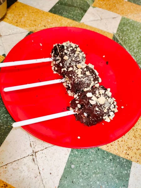 The closeup of three chocolate cake pops on a red plate  seasoned with crumbs