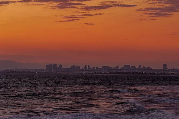 橙色日落天空下的海浪顶视图 背景为城市天际线 — 图库照片