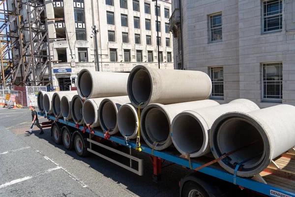 A large batch of concrete drainage pipes being delivered to a building site on a flat bed truck