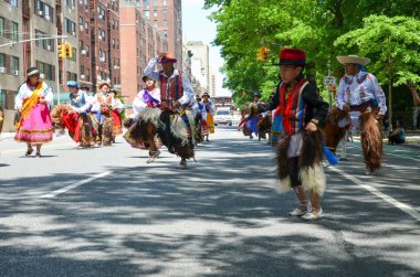 Bir grup çocuk ve yetişkin, ABD 'nin yıllık Ekvador Bağımsızlık Günü Geçidi sırasında New York' un batısında Central Park 'ta dans ediyor ve yürüyüş yapıyorlar.